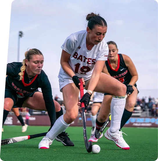 Bates field hockey player controlling the ball between two defenders